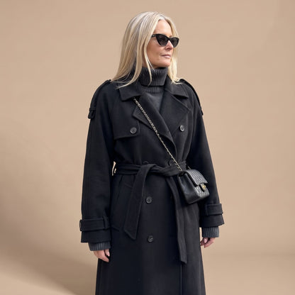 Zwarte trenchcoat gestyled over jeans voor een casual look