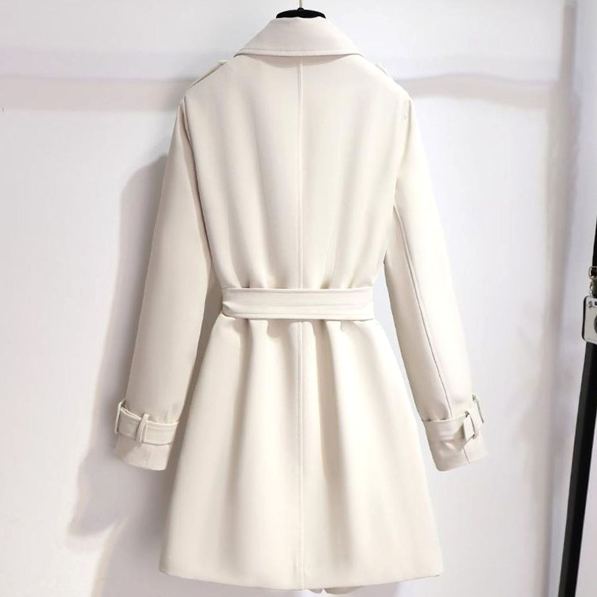 Detail van goudkleurige knopen en verstelbare ceintuur op witte trenchcoat